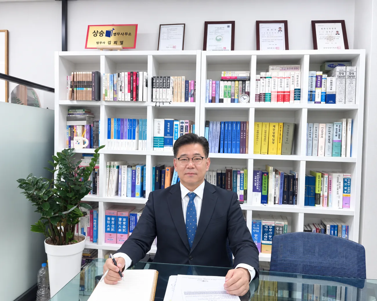 상승법무사사무소 명패와 책장 앞 책상에 앉은 김희엽 법무사
